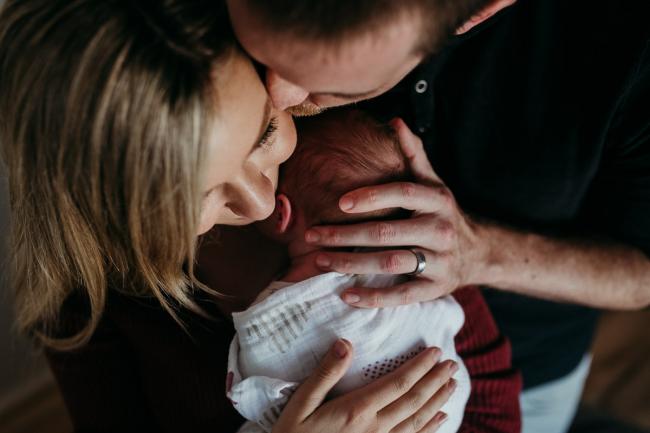 Close up of mother holding her new baby as dad kisses mum and has his hand on baby's back during a Perth newborn lifestyle session
