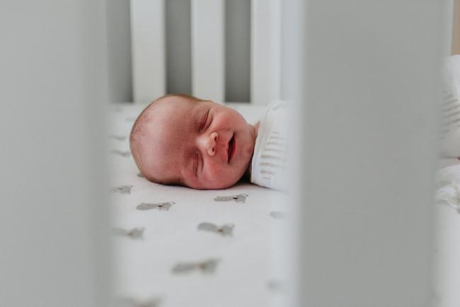Newborn-Photographer-Perth-35-of-37 Newborn baby smiling through the cot railings during a Perth newborn lifestyle session