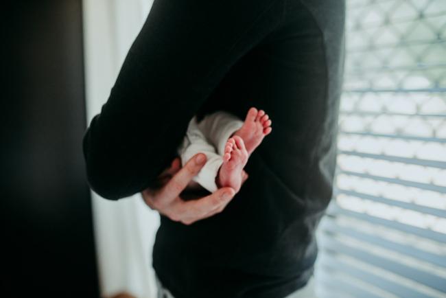 Newborn-Photographer-Perth-4-of-37 Newborn baby feet poking out from her fathers arms with Perth lifestyle newborn photographer