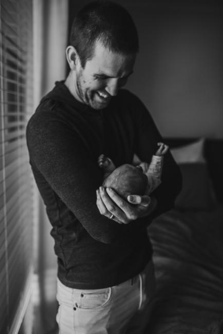 Black and white image of a father holding his new baby and smiling during a Perth newborn lifestyle session
