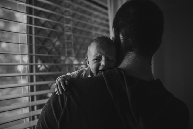 Newborn-Photographer-Perth-7-of-37 Black and white image of a new baby crying over her father's shoulder during a Perth newborn lifestyle session