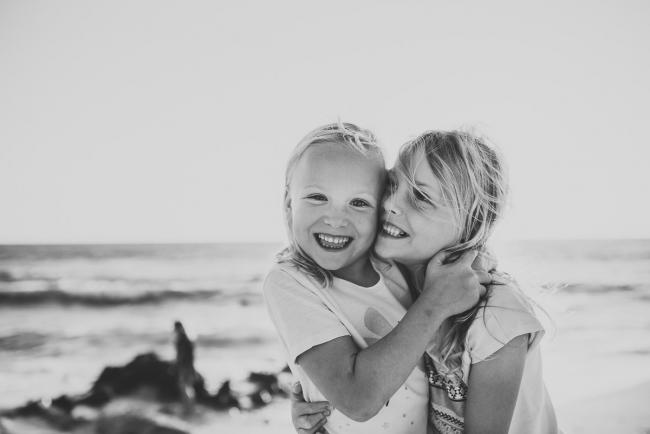Black and white image of two sisters laughing and hugging at Burns Beach during a Perth family photography session
