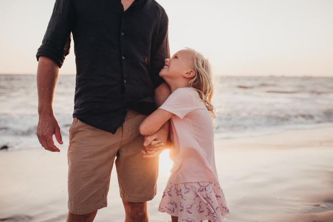 Little girl hugging her dad's arm and smiling up at him during golden hour at at Burns Beach during a Perth family photography session