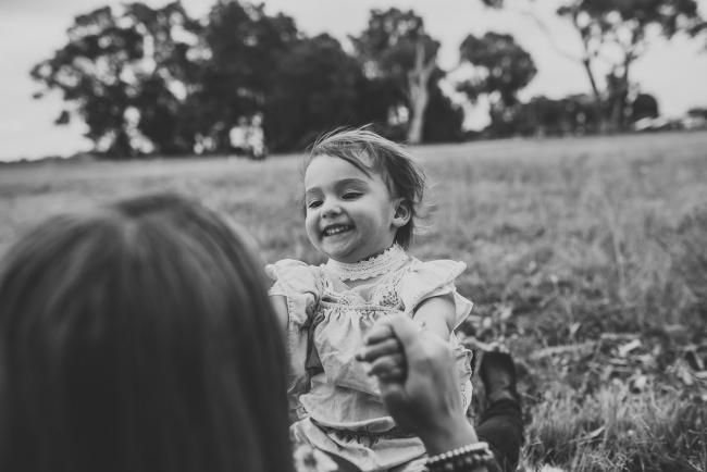 Black and white image of little girl sitting on her mother's lap and laughing with Perth family photographer at Perry's Paddock