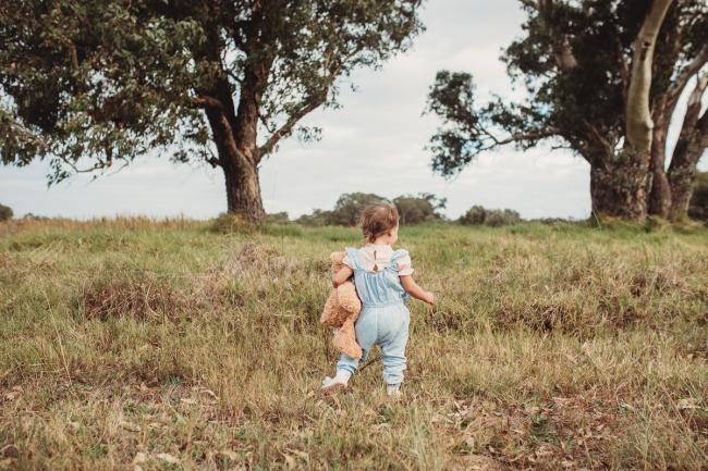 The back of a little girl as she walks towards trees holding her teddy with Perth family photographer at Perry's Paddock