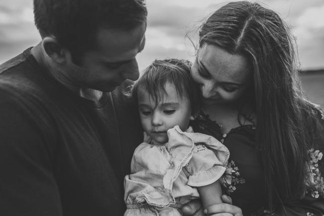 Black and white image of little girl being held by her parents with Perth family photographer at Perry's Paddock
