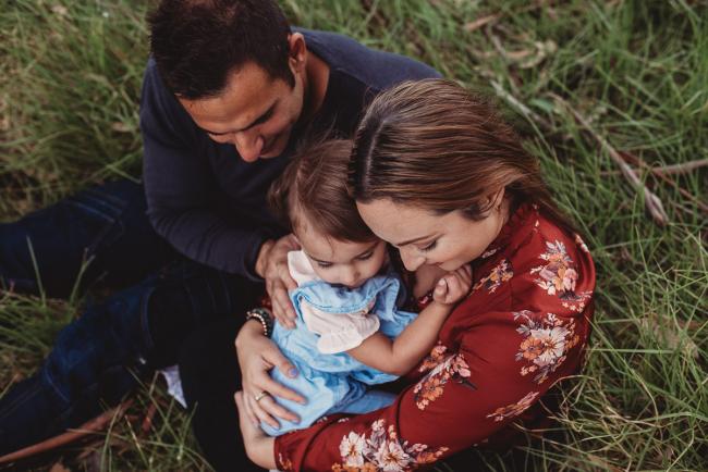 Top down image of parents cuddling their little girl whilst sitting on the grass with Perth family photographer at Perry's Paddock
