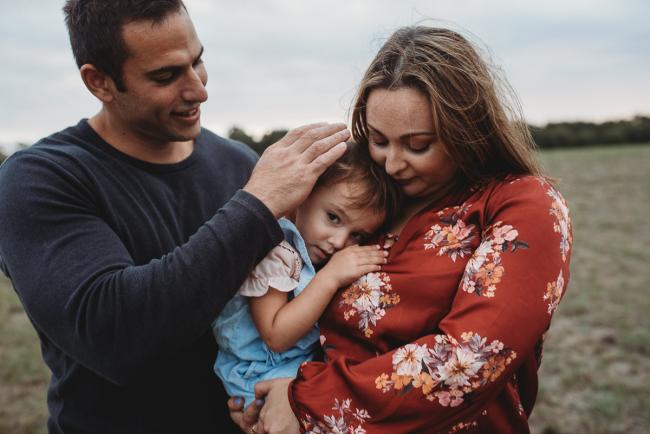 Little girl cuddling in to her mother as her father touches her head with Perth family photographer at Perry's Paddock