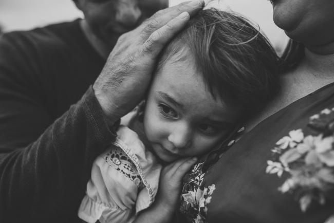 black and white image of father touching the head of his daughter as she cuddles into her mother with Perth family photographer at Perry's Paddock