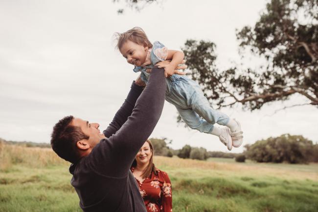 Mother smiling on as father flies their daughter in the air with Perth family photographer at Perry's Paddock