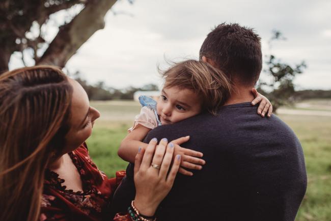 Mother touching her daughter's hand as the daughter cuddles her father with Perth family photographer at Perry's Paddock