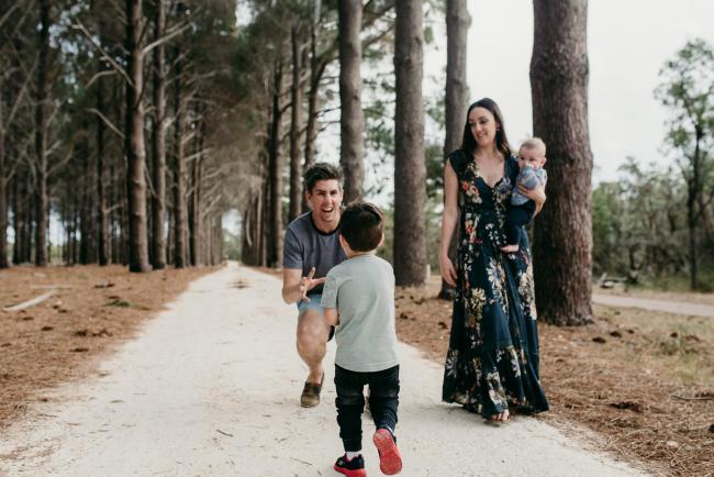Family-Photographer-Perth-The-Pines-12-of-21 Little boy running into his dad's arms as mother and baby look on during a Family photographer session at The Pines in Wanneroo