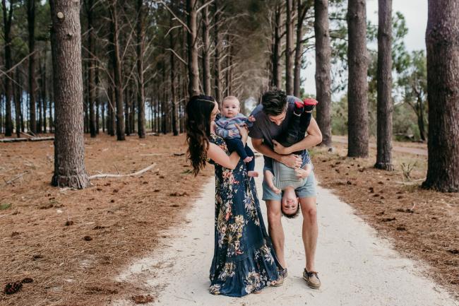 Family-Photographer-Perth-The-Pines-18-of-21 Mother holding her baby and dad holding their little boy upside down during a Family photographer session at The Pines in Wanneroo