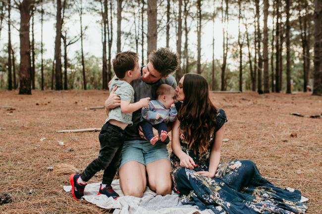 Family-Photographer-Perth-The-Pines-3-of-21 Little boy kissing his father, and mother kissing the baby during a Family photographer session at The Pines in Wanneroo