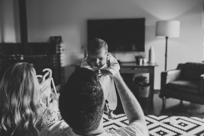 Black and white image of father lifting his new baby in the air during an in-home Perth newborn lifestyle session