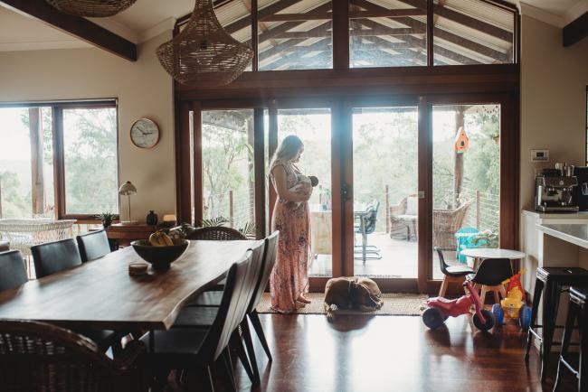 Mother standing by a window breastfeeding as their dog sits at her feet during an in-home Perth newborn lifestyle session