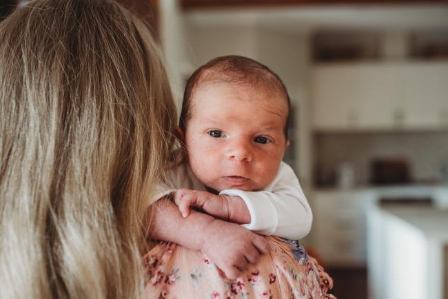 Baby peeking over the shoulder of his mother during an in-home Perth newborn lifestyle session