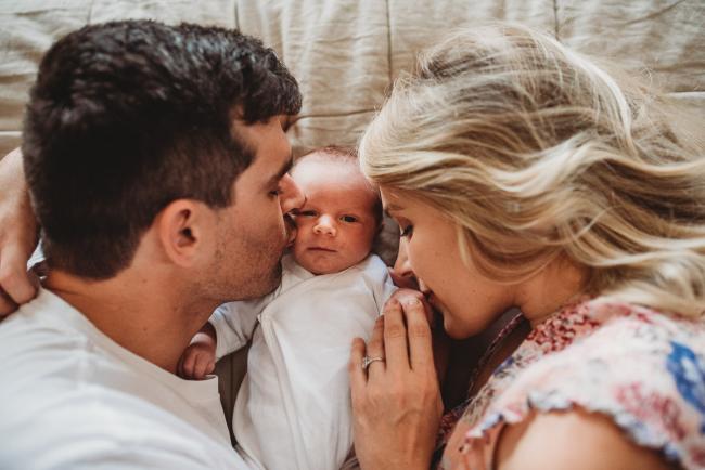 Mother and father kissing their new baby as he lays on the bed between them during an in-home Perth newborn lifestyle session