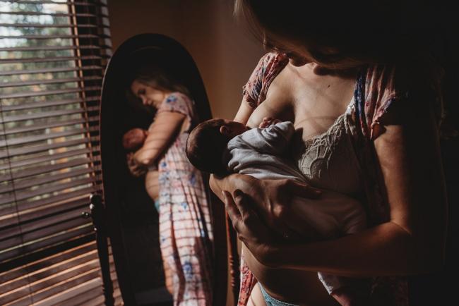 Mother breastfeeding her new baby in front of a mirror during an in-home Perth newborn lifestyle session