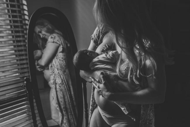 Black and white image of mother breastfeeding her new baby in front of a mirror during an in-home Perth newborn lifestyle session
