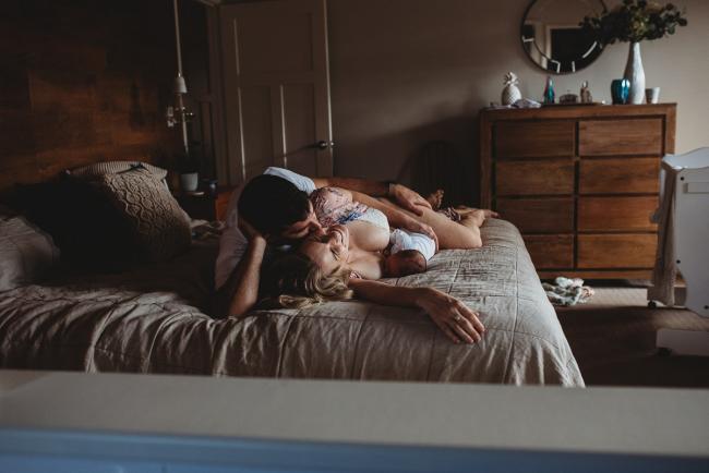 Parents laying on the bed as mum breastfeeds their new baby during an in-home Perth newborn lifestyle session
