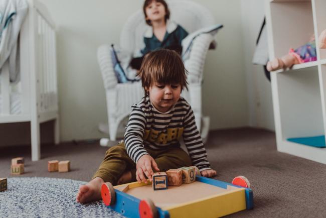 Little boy playing with blocks on the floor as older boy sits in chair behind him with Perth family photographer