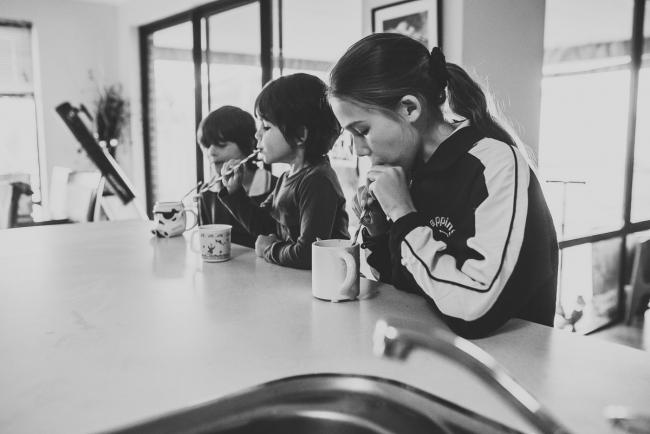 Black and white image of three kids drinking at the kitchen bench with Perth family photographer