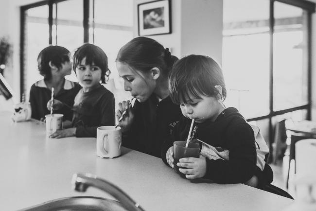 Black and white image of four kids at the kitchen bench drinking hot chocolates through straws with Perth family photographer