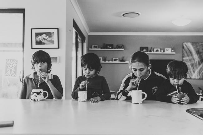 Black and white image of four kids at the kitchen bench drinking hot chocolates through straws with Perth family photographer