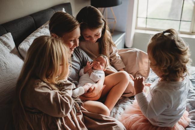 Boy holding his baby sister and surrounded by his other sisters during a Perth Newborn photography session