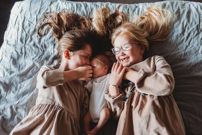 New baby laying between her two sisters during a Perth Newborn photography session