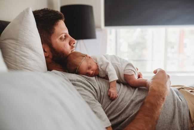 Father laying on the bed with his new baby on his chest during a Perth Newborn photography session