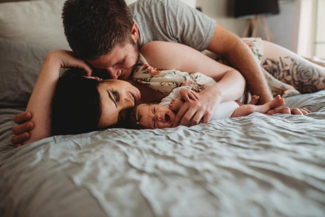 Parents laying on the bed with their new baby during a Perth Newborn photography session