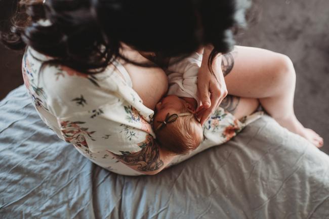 Top down image of mother sitting on the edge of the bed and breastfeeding her new baby during a Newborn lifestyle photographer Perth session