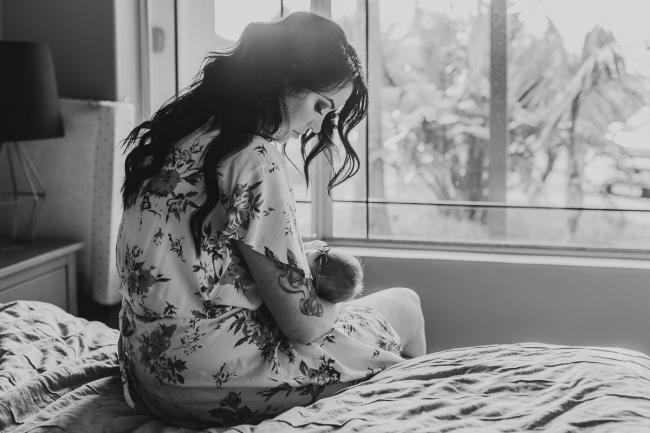 black and white image of mother sitting on the bed breastfeeding during a Perth Newborn photography session