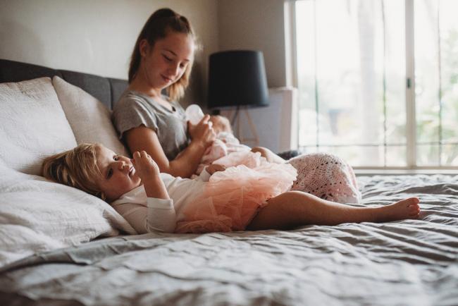 Girl feeding her niece on the bed while her other niece sits next to her during a Newborn lifestyle photographer Perth session