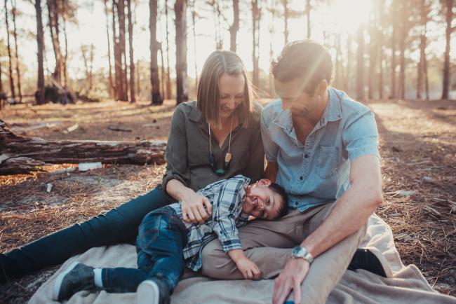 Little boy laying across the lap of his parents during a Perth maternity photography session at The Pines at golden hour