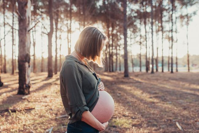 Pregnant woman looking down at her bare belly during a Perth maternity photography session at The Pines at golden hour