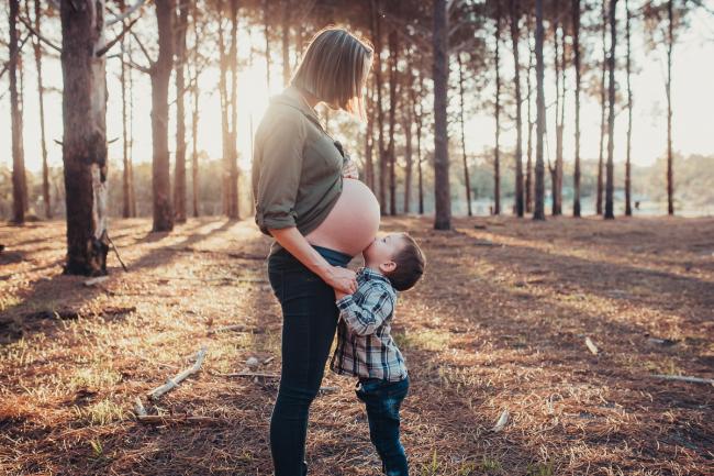 Little boy kissing his mother's bare pregnant tummy during a Perth maternity photography session at The Pines at golden hour