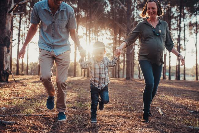 Parents running with their son who is laughing during a Perth maternity photography session at The Pines at golden hour