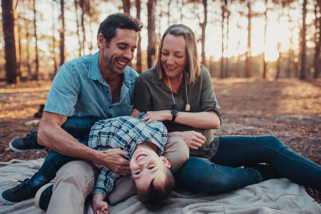 Parents with their son laying upside down on their lap during a Perth maternity photography session at The Pines at golden hour