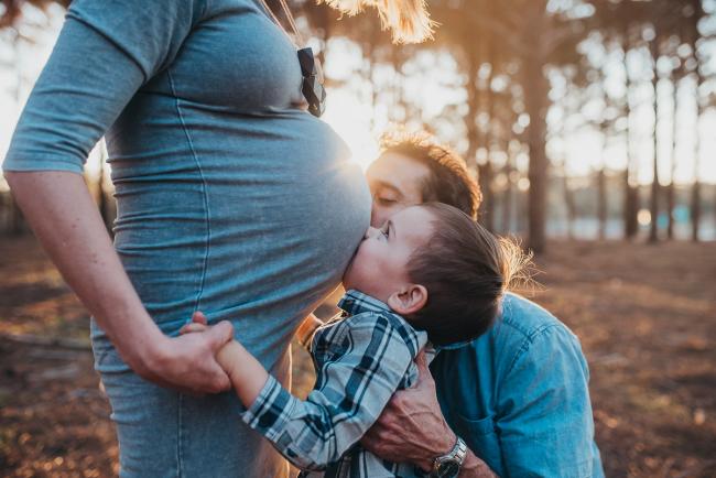 Father and son kissing mother's pregnant tummy during a Perth maternity photography session at The Pines at golden hour