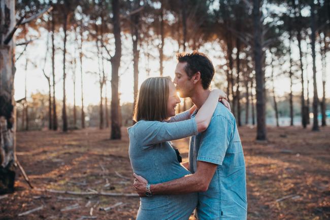 Husband kissing the forehead of his pregnant wife during a Perth maternity photography session at The Pines at golden hour
