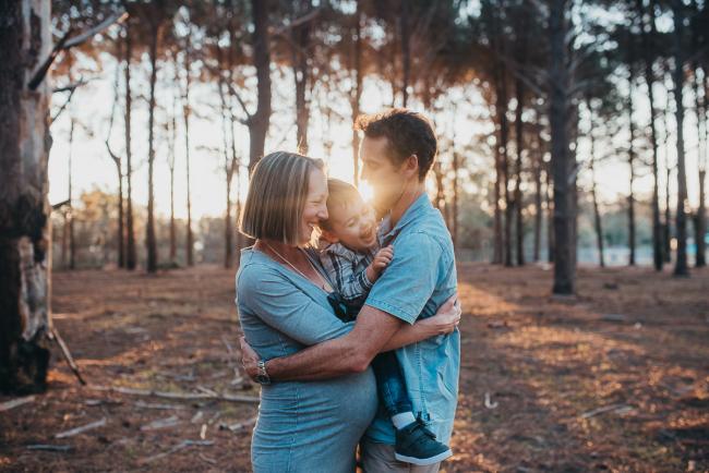 Pregnant couple embracing their son during a Perth maternity photography session at The Pines at golden hour