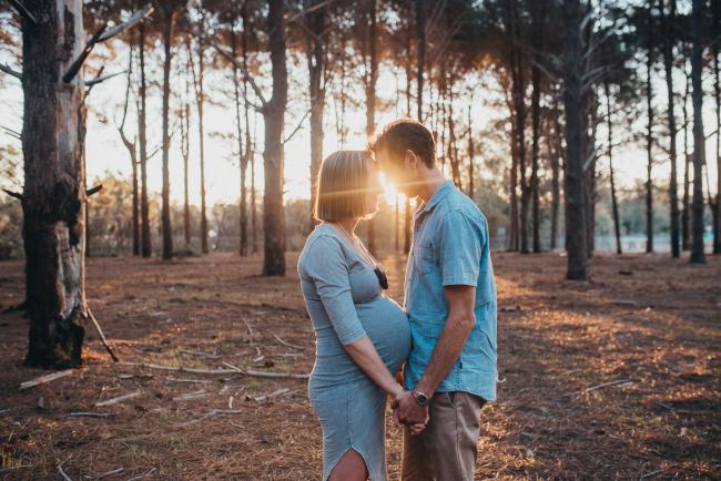 Pregnant couple facing each other, holding hands and touching foreheads during a Perth maternity session at The Pines during Golden Hour