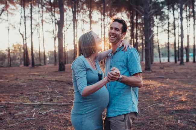 Pregnant couple laughing and dancing during a Perth maternity photography session at The Pines at golden hour