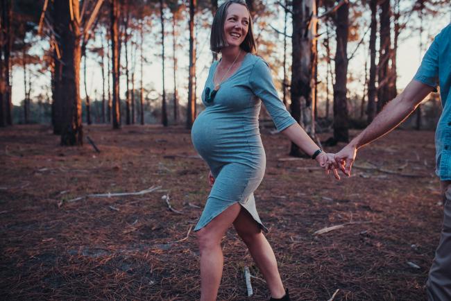 Pregnant mother looking back and smiling at her husband during a Perth maternity session at The Pines during Golden Hour
