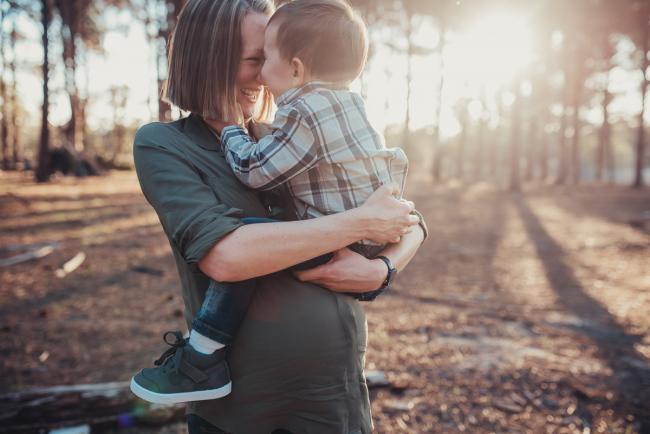 Little boy being held on top of his mother's pregnant tummy during a Perth maternity photography session at The Pines at golden hour