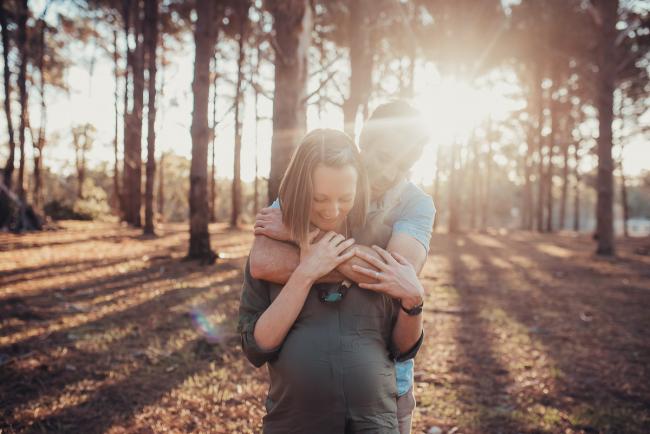 Husband hugging his wife from behind during a Perth maternity photography session at The Pines at golden hour