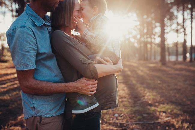 Pregnant mother holding her son on top of her bump as dad hugs them from behind during a Perth maternity session at The Pines during Golden Hour